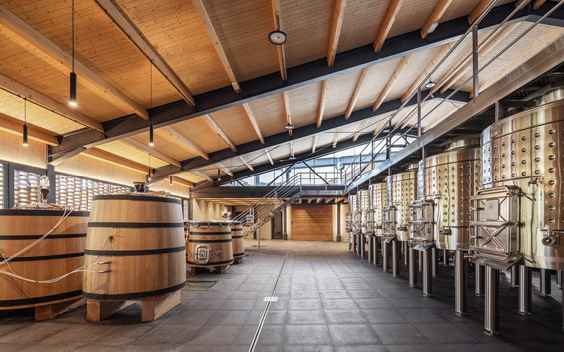 Color image of the inside of production facility with steel tanks and wooden barrels.
